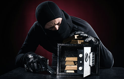 Maskierter Dieb mit Waffe öffnet einen Tresor mit Gold