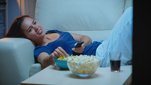 Frau entspannt auf Couch und schaut Fernsehen